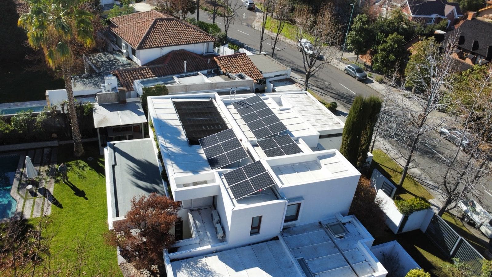 Vista aérea de una casa blanca de techo plano con paneles solares, rodeada de árboles en un barrio residencial