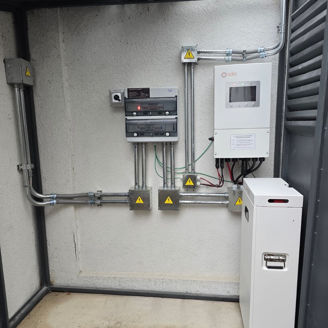 Tablero fotovoltaico con su placa, inversor con el procedimiento de desconexión en la tapa, cajas con señalética de peligro y una batería al lado