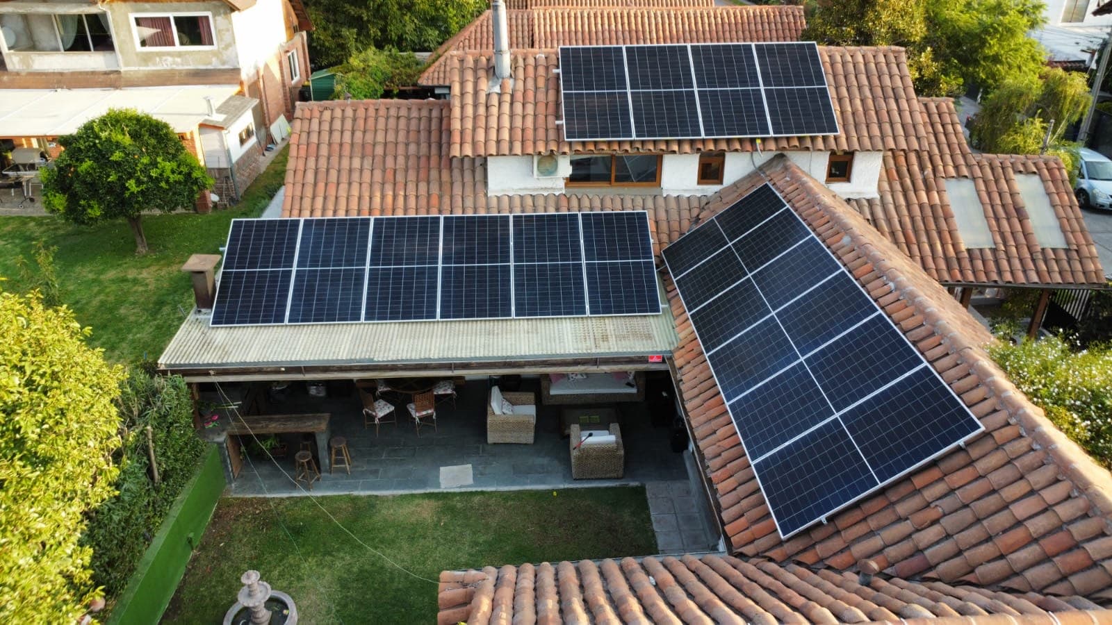 Vista aérea de una casa con techo de tejas de arcilla y tres grupos de paneles solares, junto a un jardín y una terraza techada
