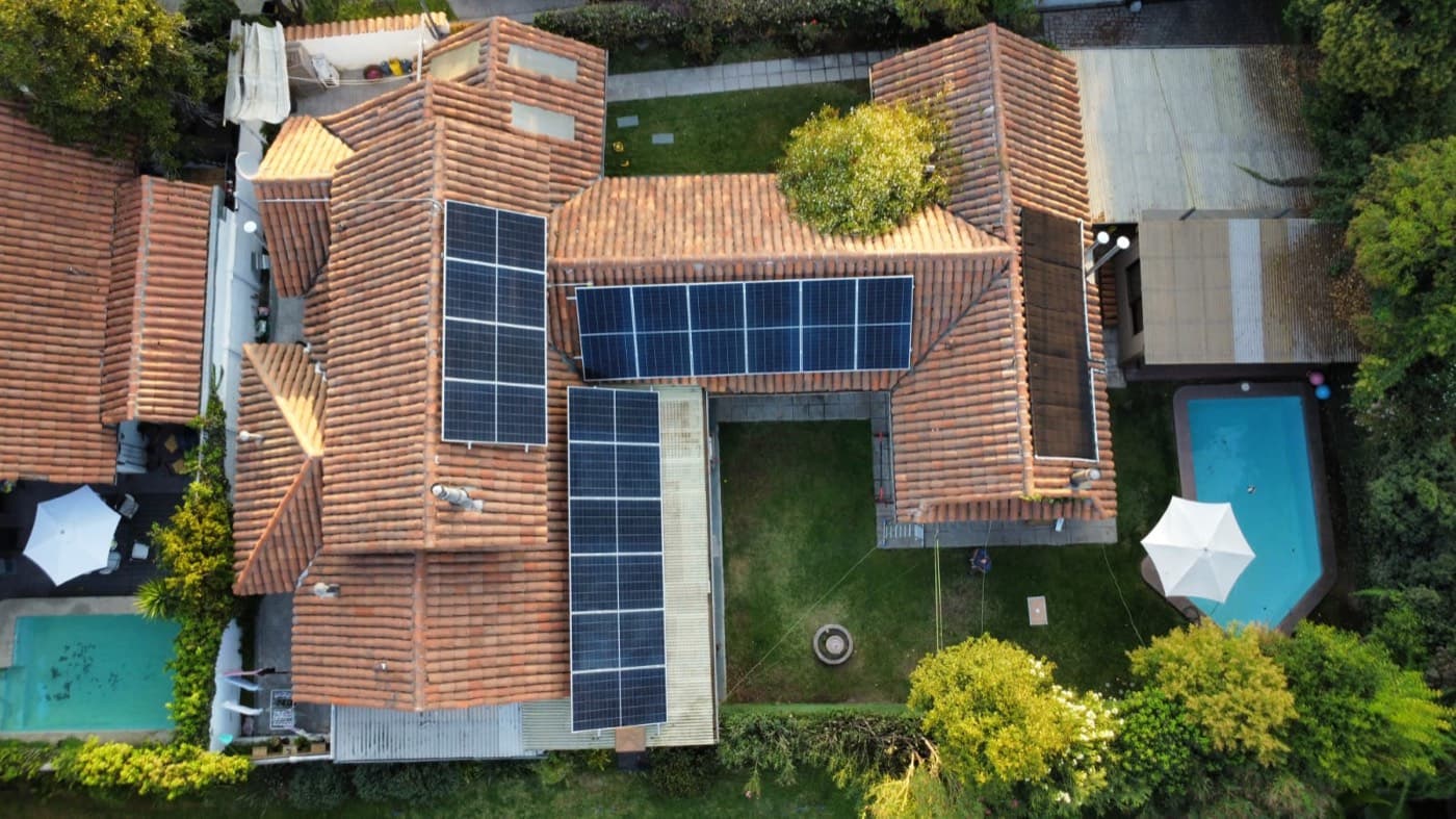 Vista aérea de una casa con techo de tejas y paneles solares en distintas aguas, con patio central y piscina