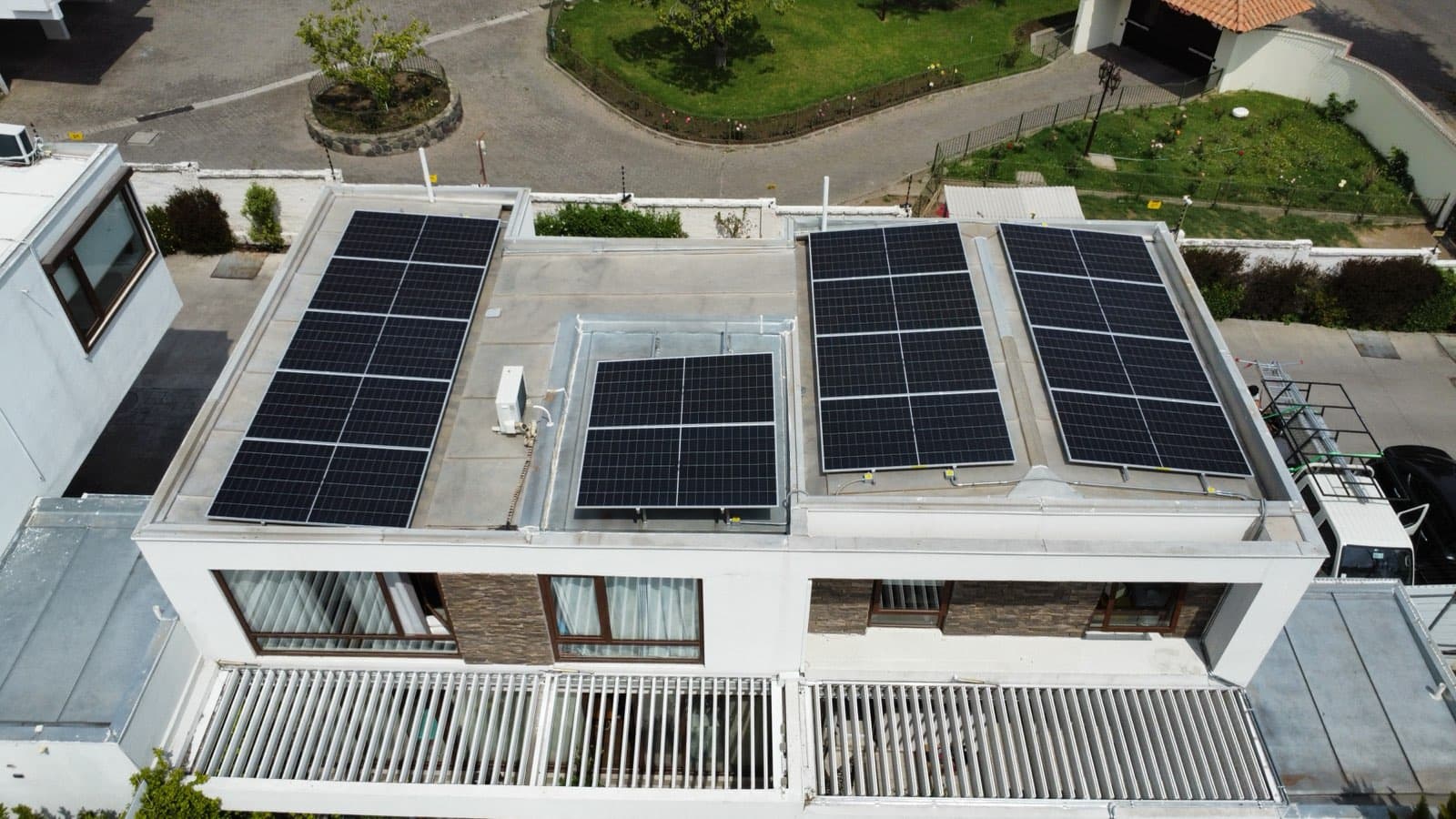 Vista aérea de una casa blanca de techo plano con cuatro grupos de paneles solares sobre la losa